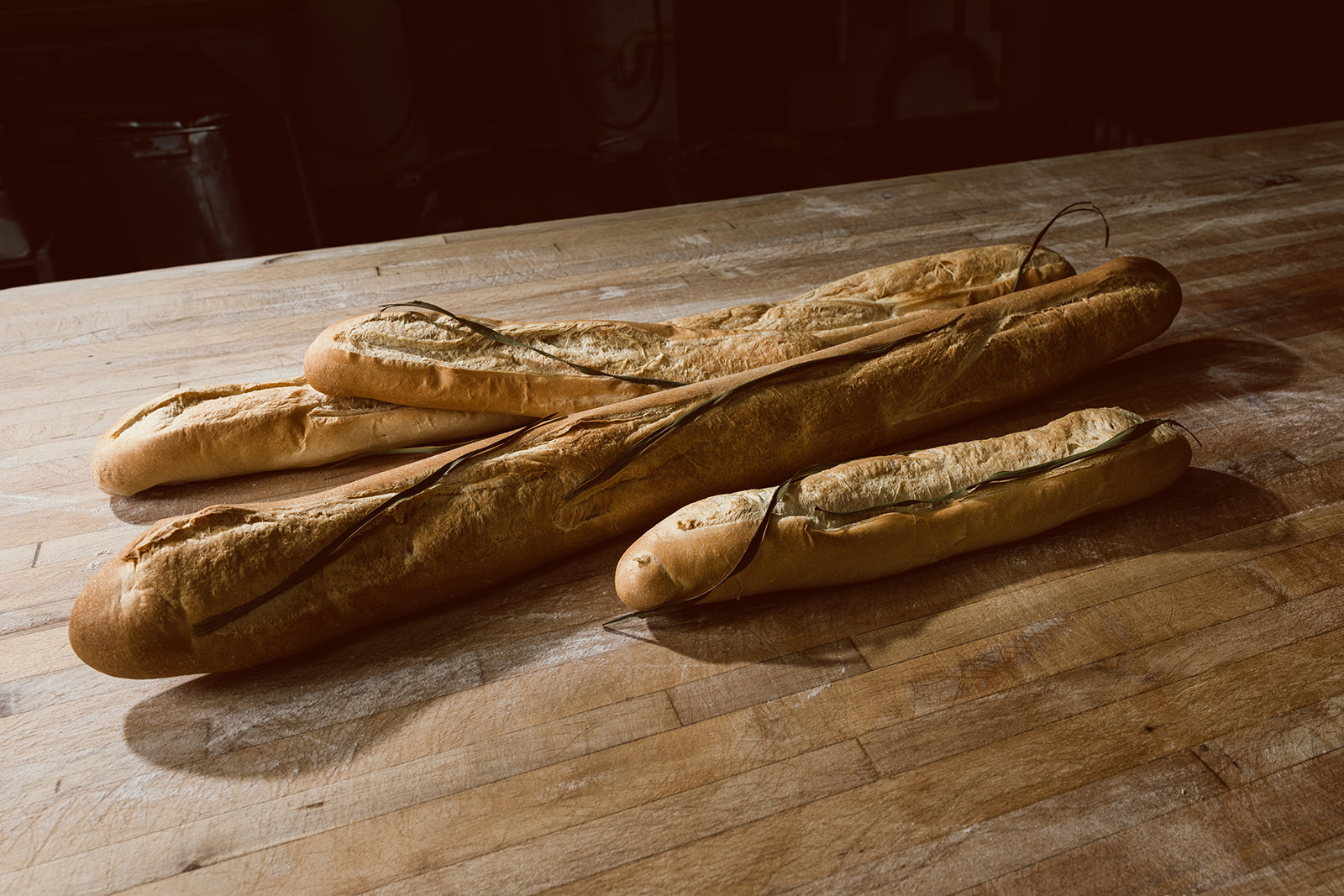 Several La Segunda Cuban bread loaves stacked across a dark butcher-block table, each with the freshly cut palmetto leaf laid down the length of the split.