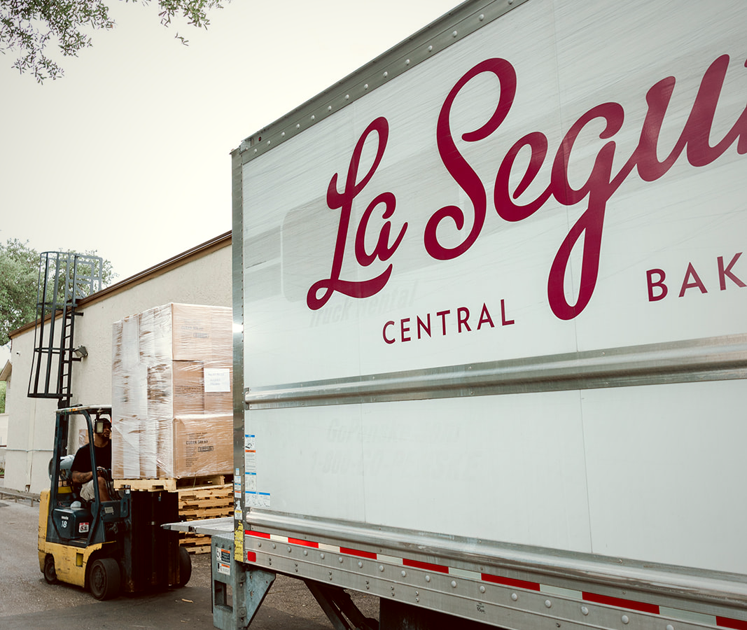 A forklift loads shrink-wrapped pallets of bread onto a La Segunda Central Bakery box truck at the Ybor City loading dock.